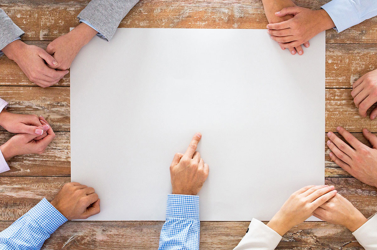 Business team brainstorming on a whiteboard, hands crossed, pointing to the center of the board.