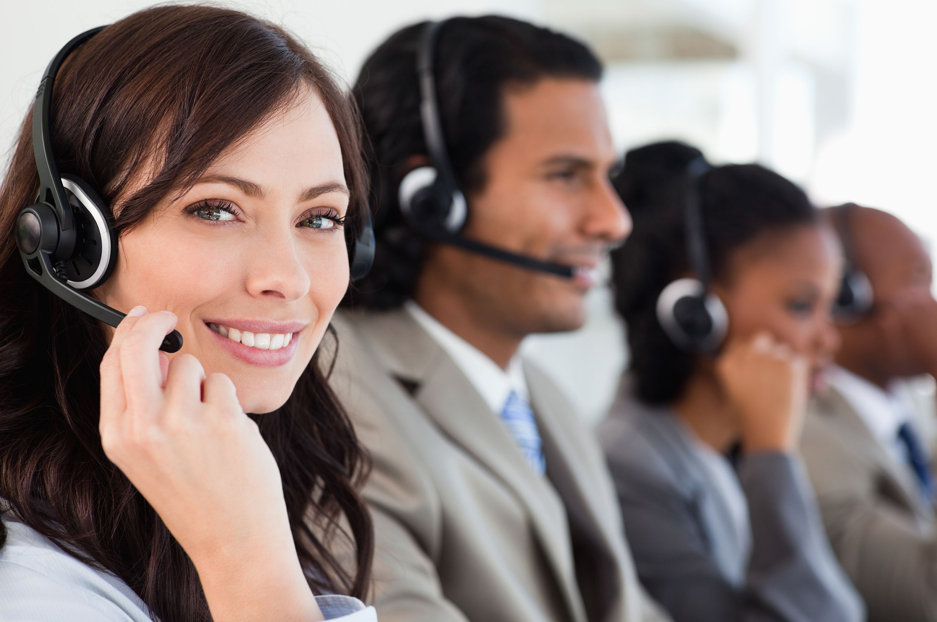 Four customer service representatives wearing headphones, with focus on a smiling woman