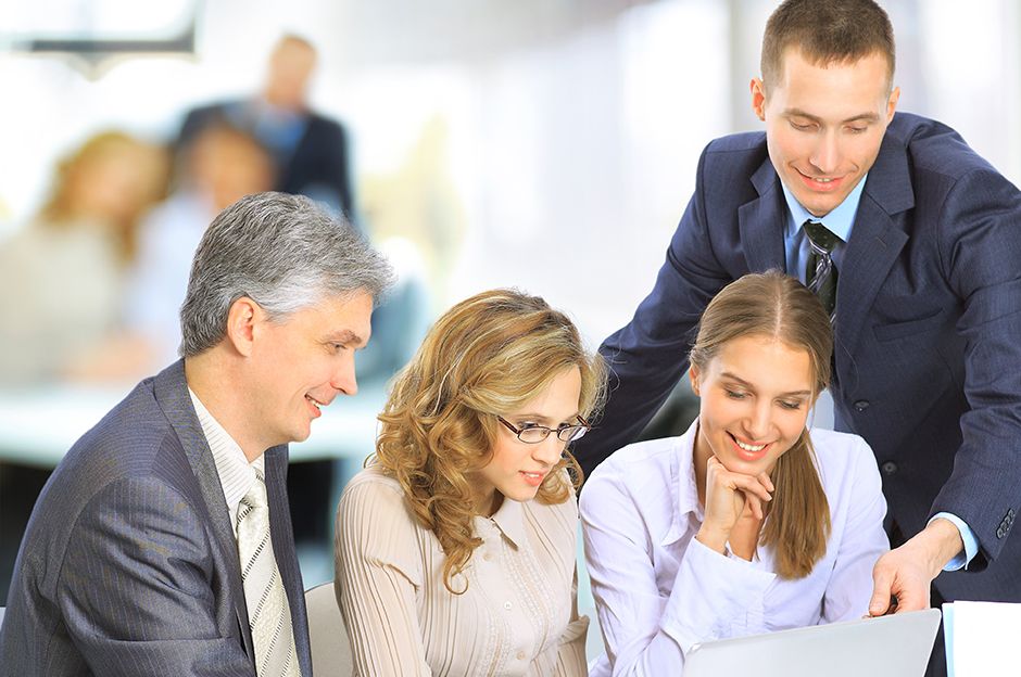 Four business professionals working together and looking at a laptop in an office setting