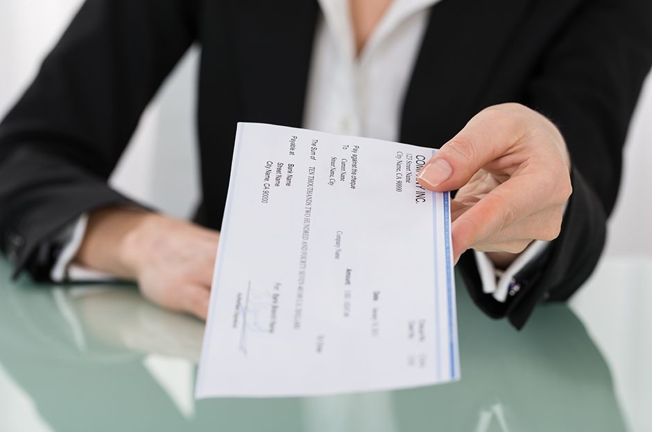 Close up of a woman in professional attire holding a check in her hand.