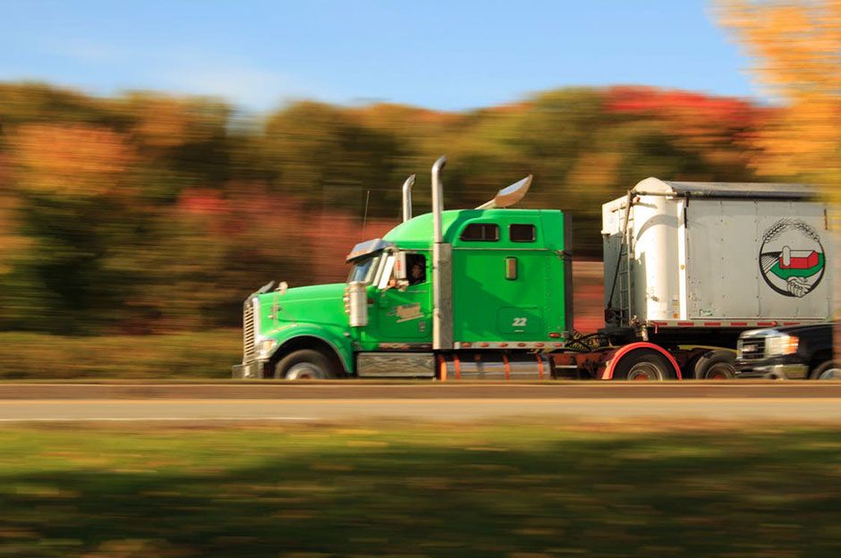 Green truck driving through autumn-colored nature with motion blur background.