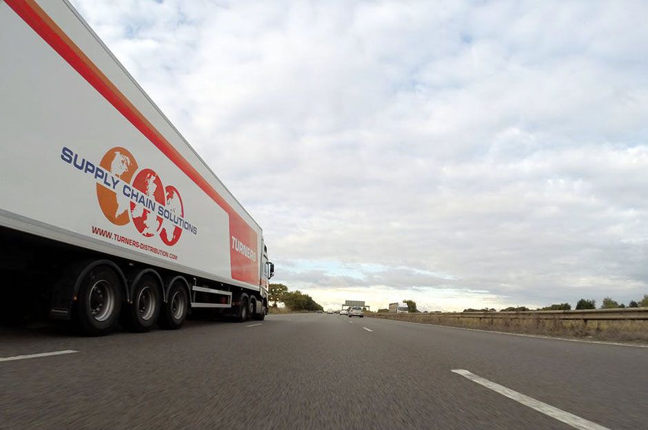 Orange and white truck displaying supply chain solutions driving on the road