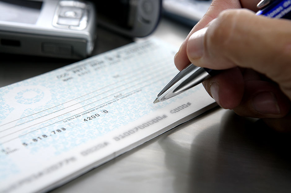 Close-up hand writing a check with pen on a checkbook, on a metal desk surface