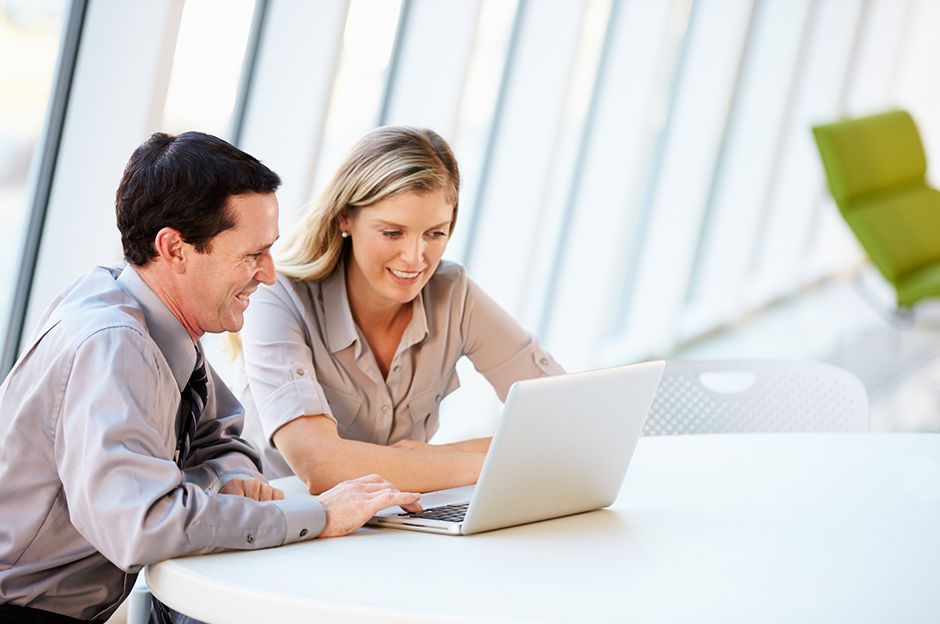 A men and a women sitting and smiling while working on a laptop together