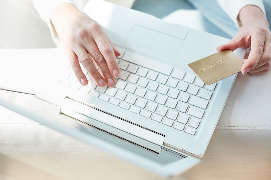 Hand holding a gold credit card with a laptop on the background, suggesting making a payment online.